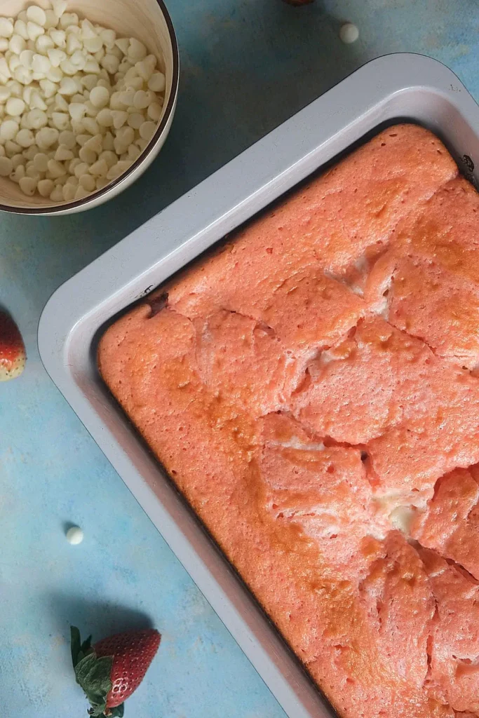 Freshly baked strawberry earthquake cake in a pan with white chocolate chips and strawberries nearby.