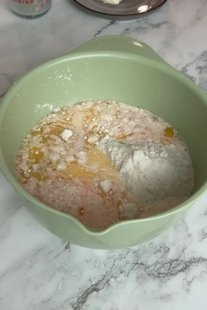 Strawberry cake mix batter with eggs, melted butter, milk, and cake mix in a light green mixing bowl on a marble countertop.