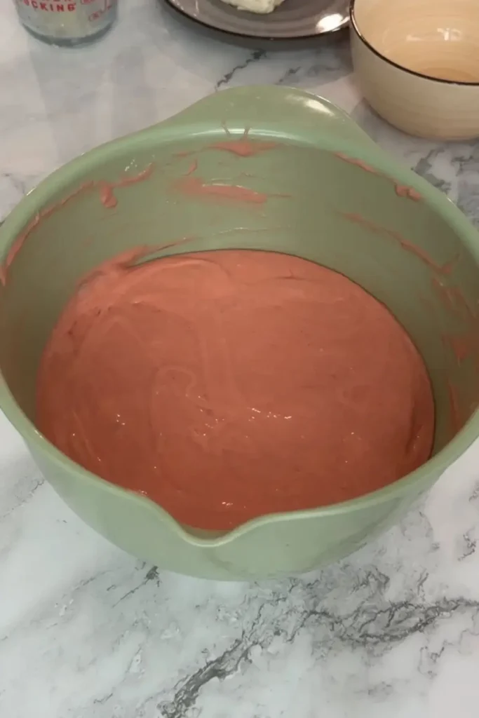 Smooth pink strawberry cake batter fully mixed in a light green bowl.
