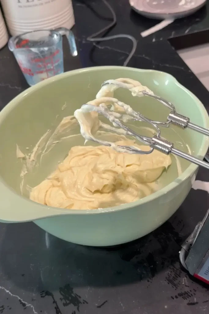 Cream cheese mixture beaten smooth with hand mixer beaters in a mixing bowl.