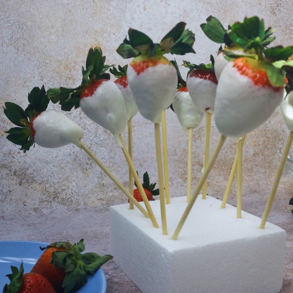 White chocolate-covered strawberries on skewers set in a foam block to dry.