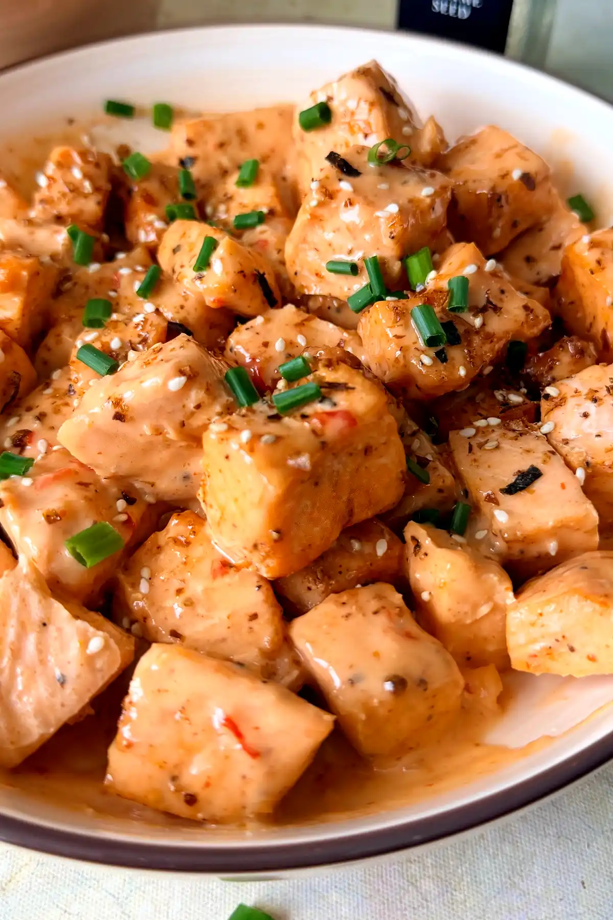 Close-up of tender air fryer bang bang salmon bites coated in creamy sweet and spicy sauce with sesame seeds and chopped green onions.
