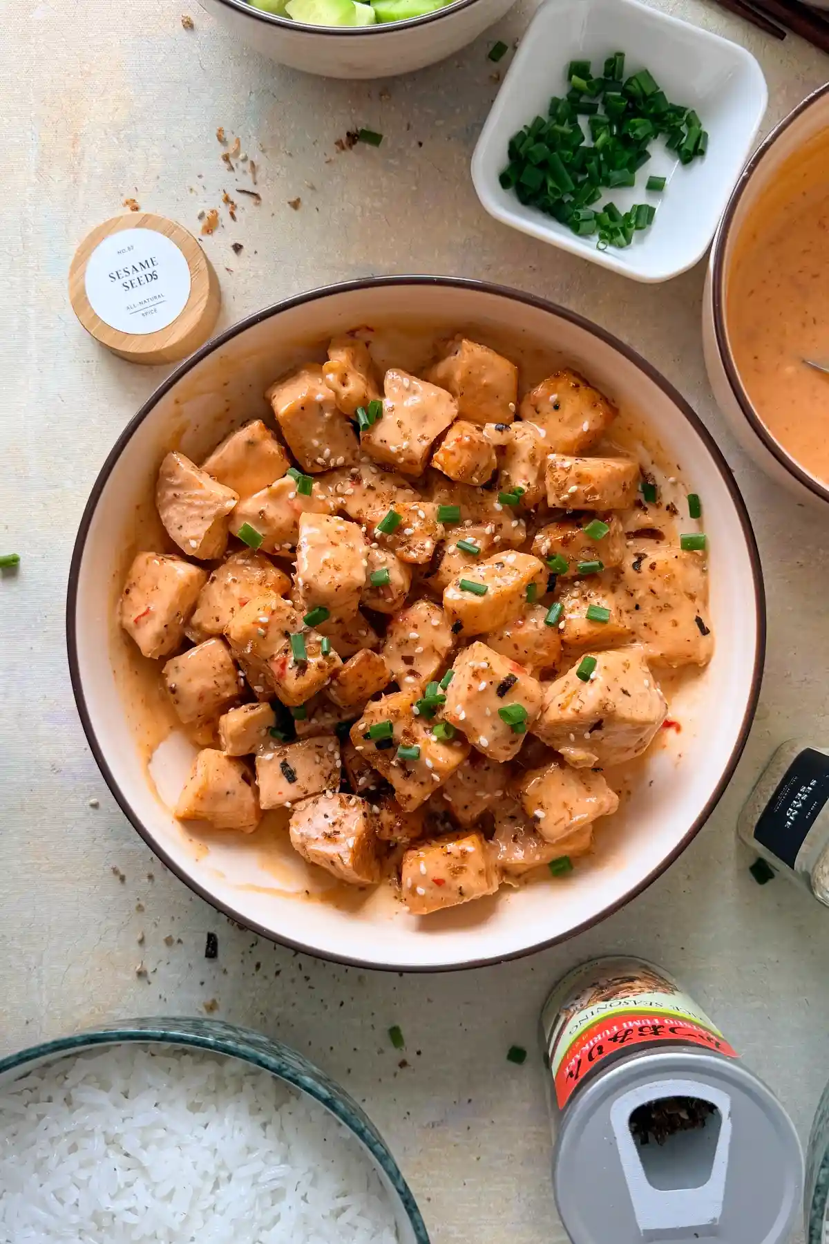 Overhead shot of air fryer bang bang salmon bites in a bowl surrounded by rice, sauce, sesame seeds, and chopped chives.