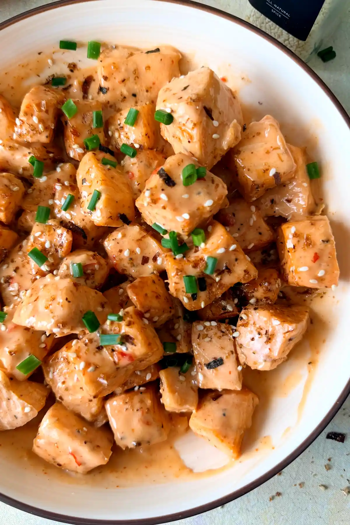 Air fryer bang bang salmon bites in a bowl, tossed in creamy bang bang sauce and topped with sesame seeds and fresh chives.