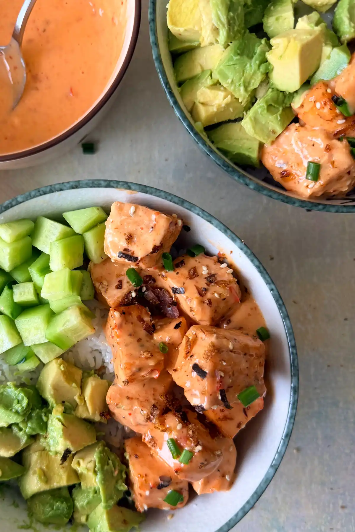 Bang bang salmon bites served over rice with avocado and cucumber in a fresh salmon rice bowl.