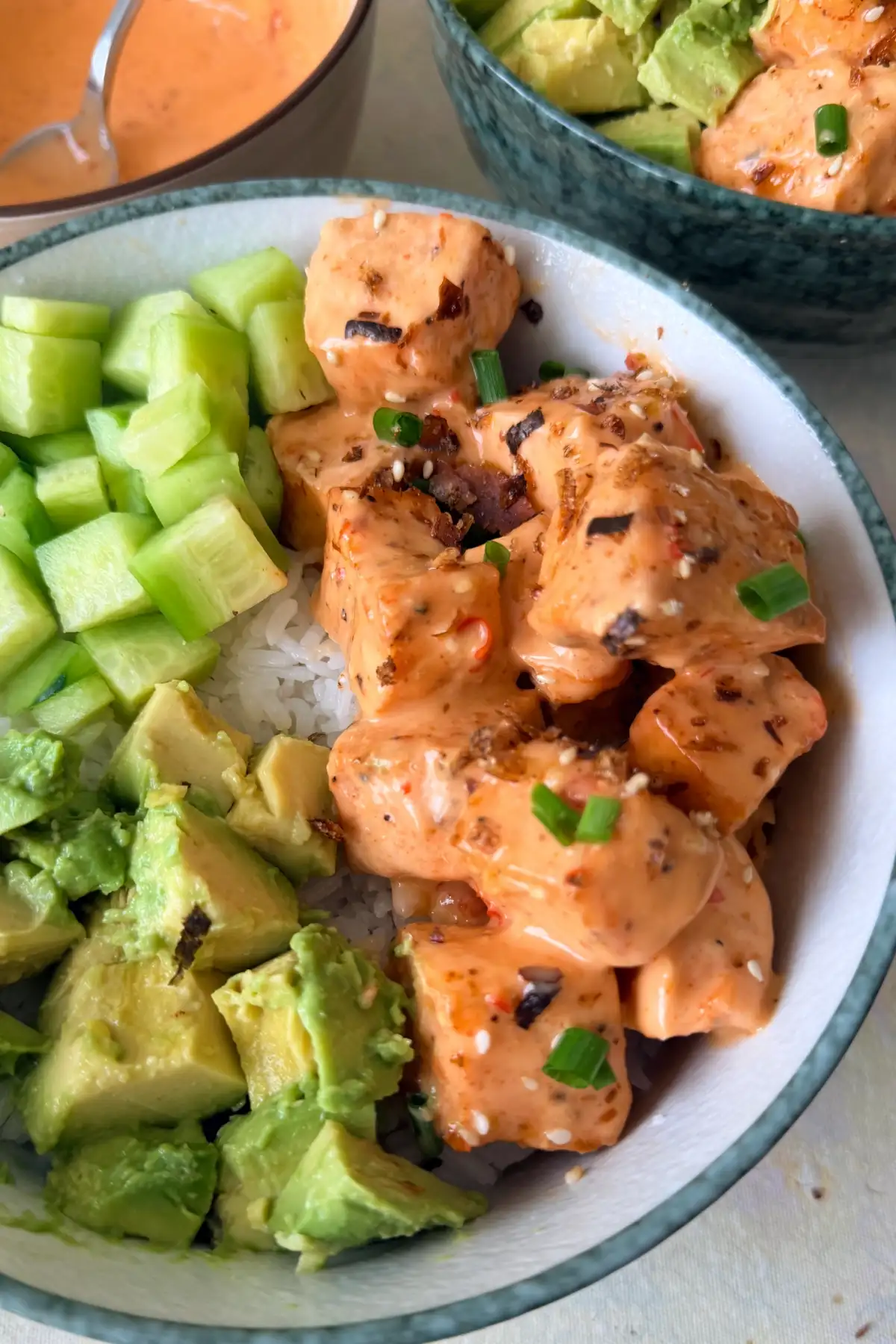 Salmon rice bowl with creamy bang bang salmon bites, diced cucumber, avocado, and white rice.