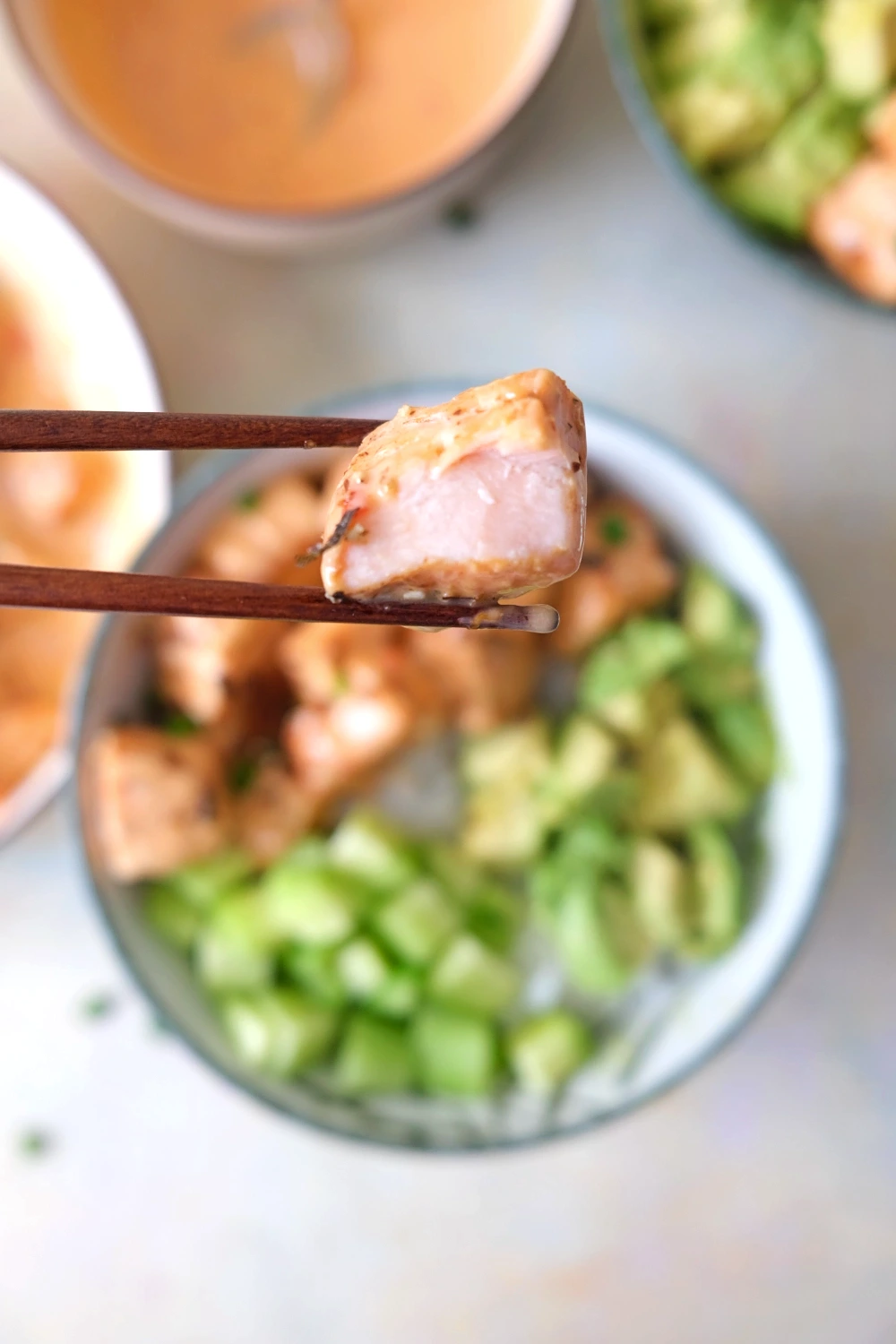 Chopsticks holding a tender bite of bang bang salmon showing the juicy interior and creamy sauce coating.