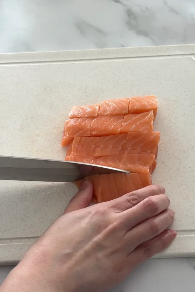 Cutting fresh salmon fillet into bite-sized cubes for air fryer salmon bites.