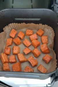 Seasoned salmon cubes arranged in a single layer in an air fryer basket lined with parchment paper.