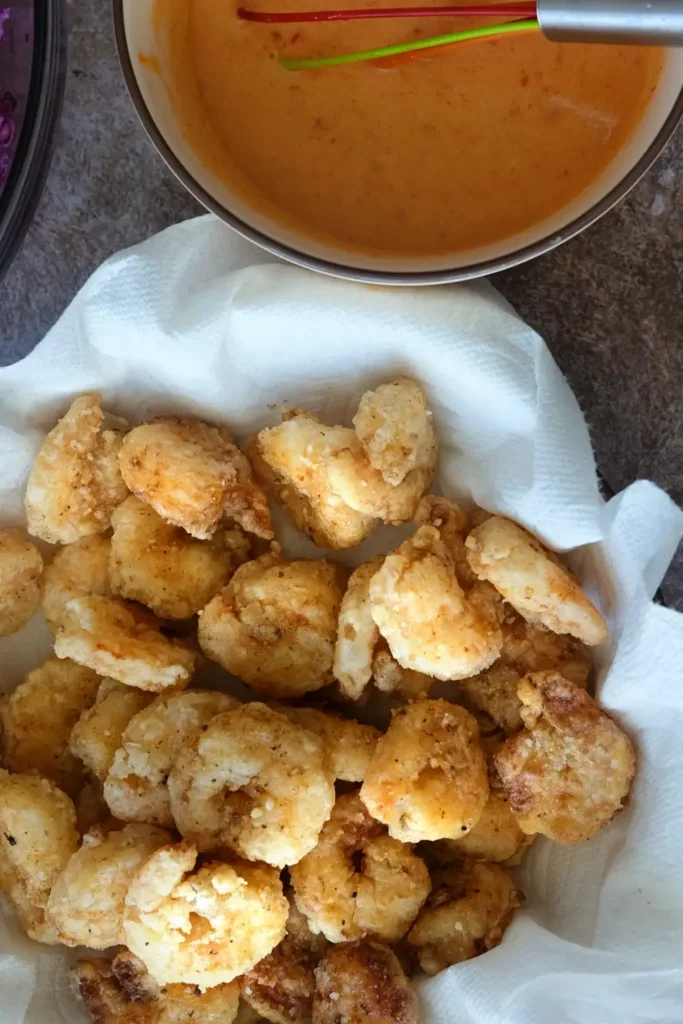 Fried shrimp resting on paper towel with bang bang sauce and cabbage slaw nearby
