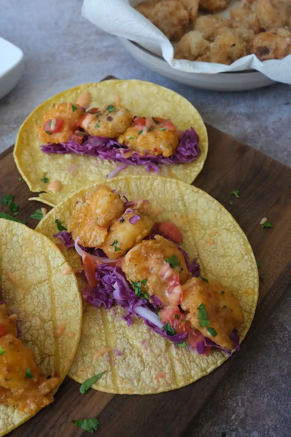 Bang bang shrimp tacos with crispy shrimp, purple cabbage, diced tomatoes, and creamy sauce on corn tortillas