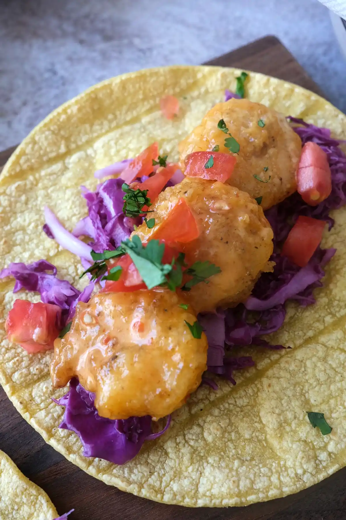 Close-up of a bang bang shrimp taco with crispy shrimp, creamy sauce, cabbage, and fresh toppings
