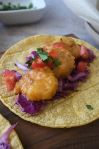 Close-up of a bang bang shrimp taco with crispy shrimp, creamy sauce, cabbage, and fresh toppings