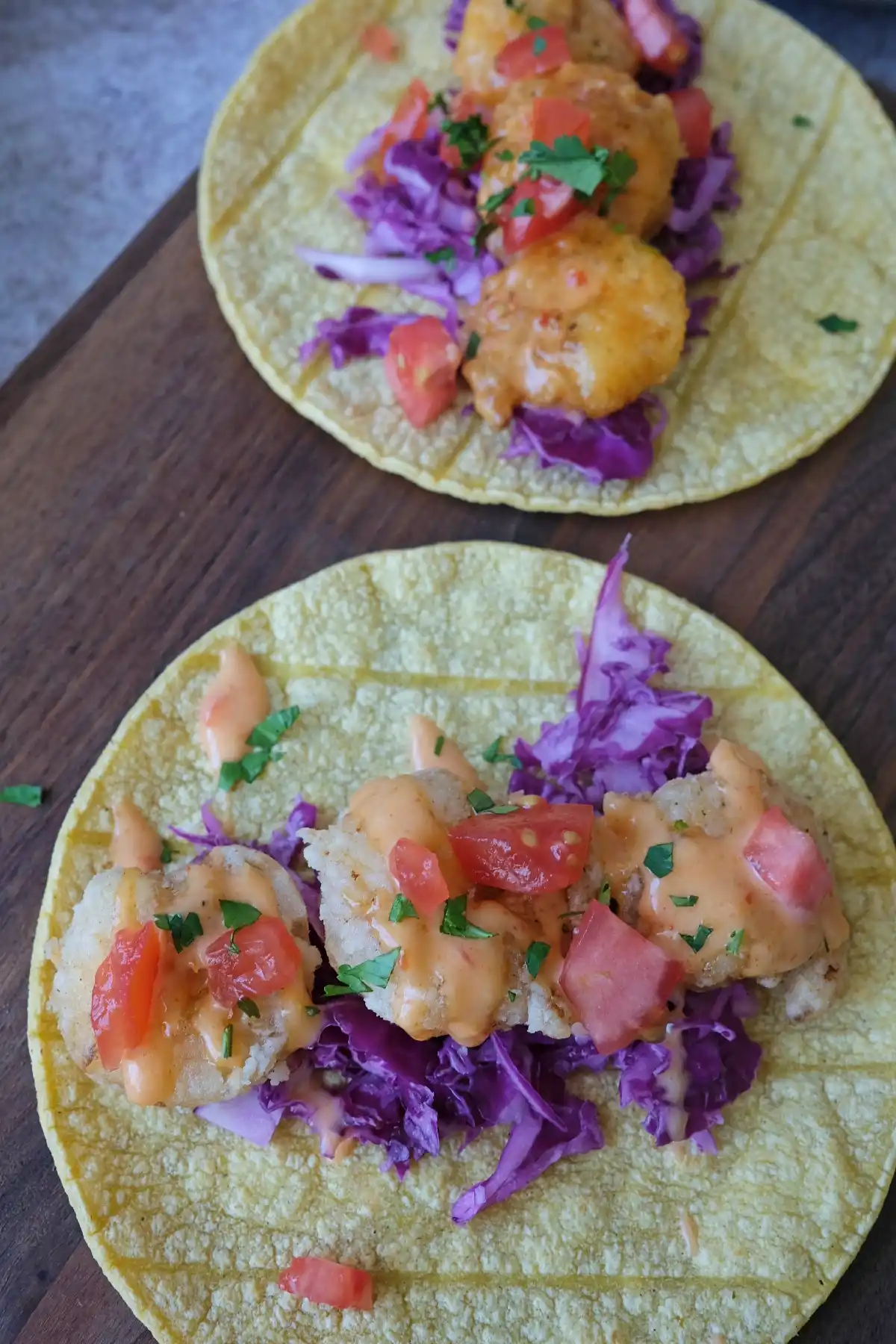 Two bang bang shrimp tacos with lightly fried shrimp, purple cabbage, tomatoes, and creamy sauce drizzle