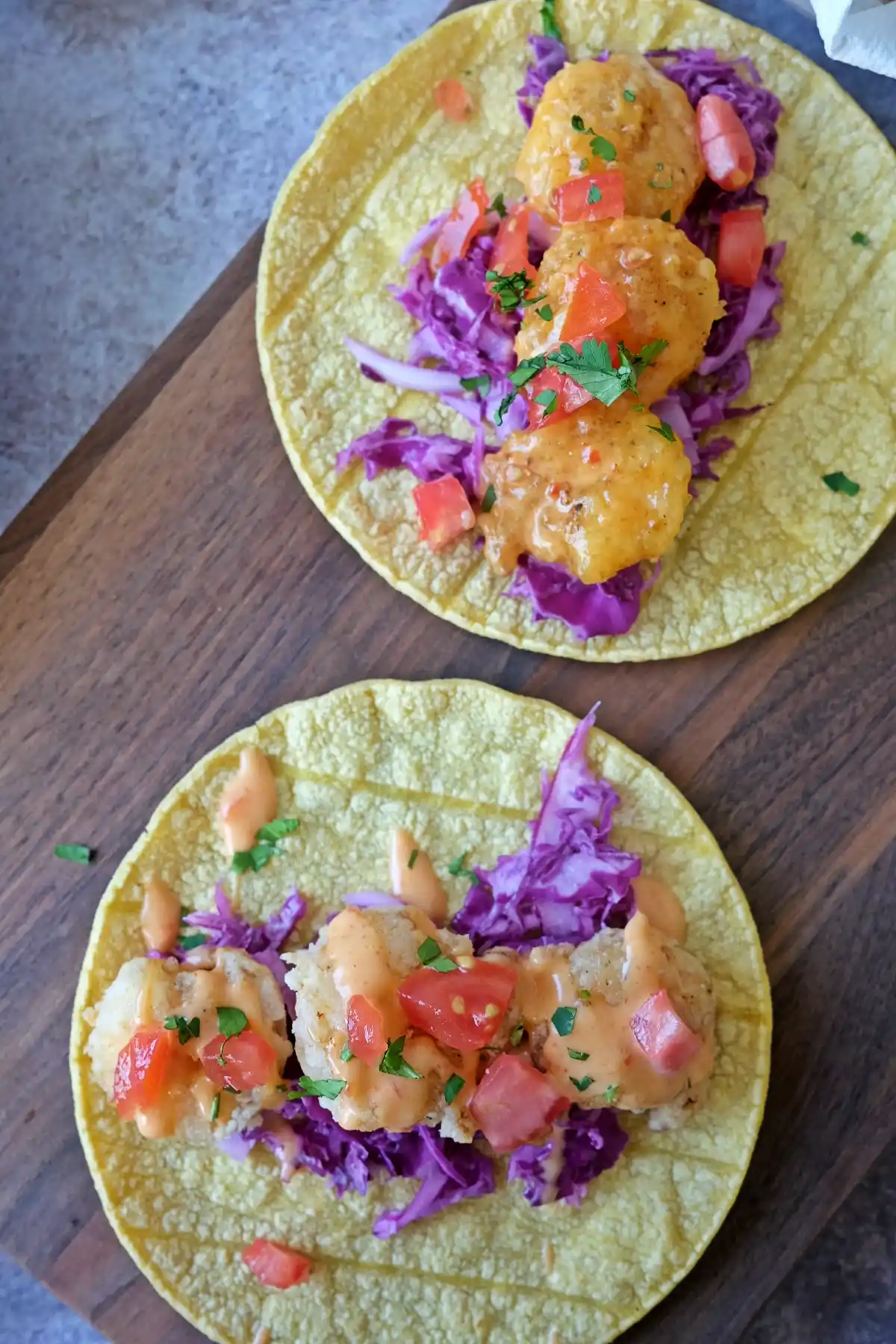 Bang bang shrimp tacos with lightly fried shrimp, purple cabbage, tomatoes, and creamy sauce drizzle