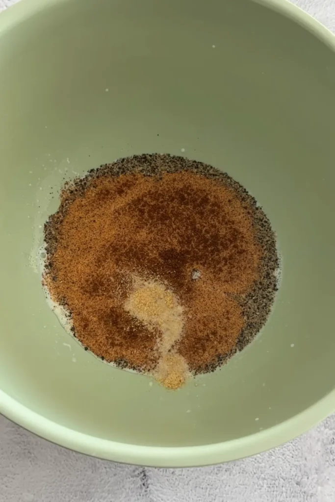 Bowl with buttermilk marinade and spices including paprika, black pepper, and onion powder