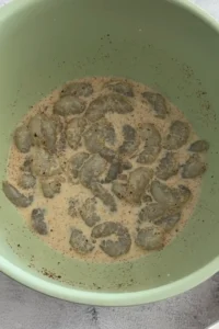 Raw shrimp soaking in seasoned buttermilk marinade in a mixing bowl