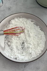 Mixing potato starch and seasoning with a whisk in a bowl for dredging shrimp