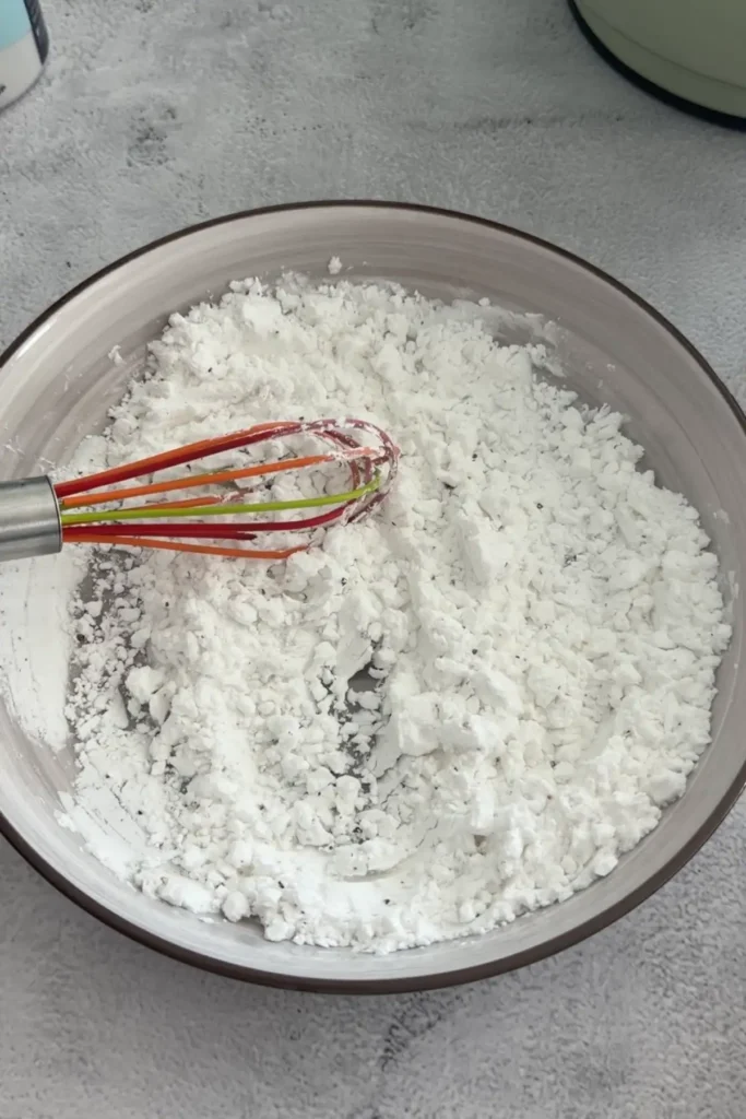 Mixing potato starch and seasoning with a whisk in a bowl for dredging shrimp