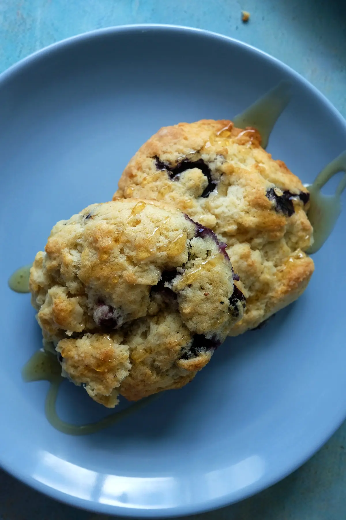 Warm blueberry biscuits drizzled with honey on a plate.