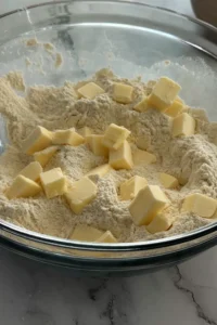 Cold butter cubes added to flour mixture for blueberry biscuits.