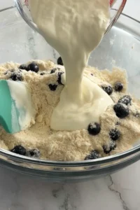 Pouring cream and vinegar mixture into blueberry biscuit dough.