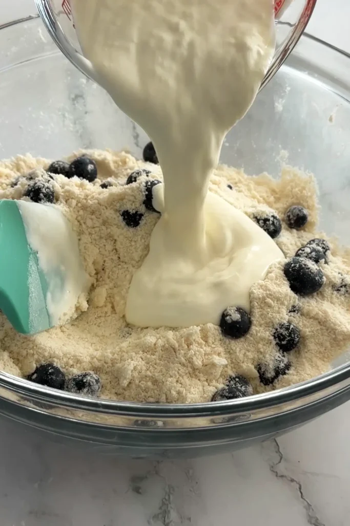 Pouring cream and vinegar mixture into blueberry biscuit dough.