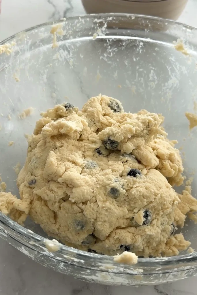 Pouring cream and vinegar mixture into blueberry biscuit dough.