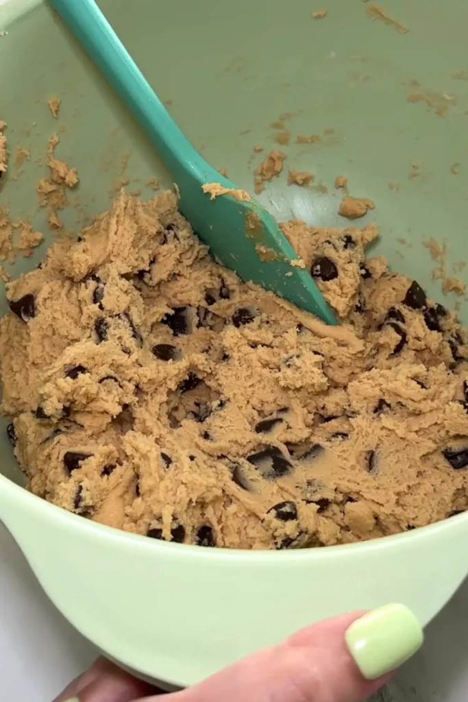 Chocolate chip cookie dough in green mixing bowl with teal spatula