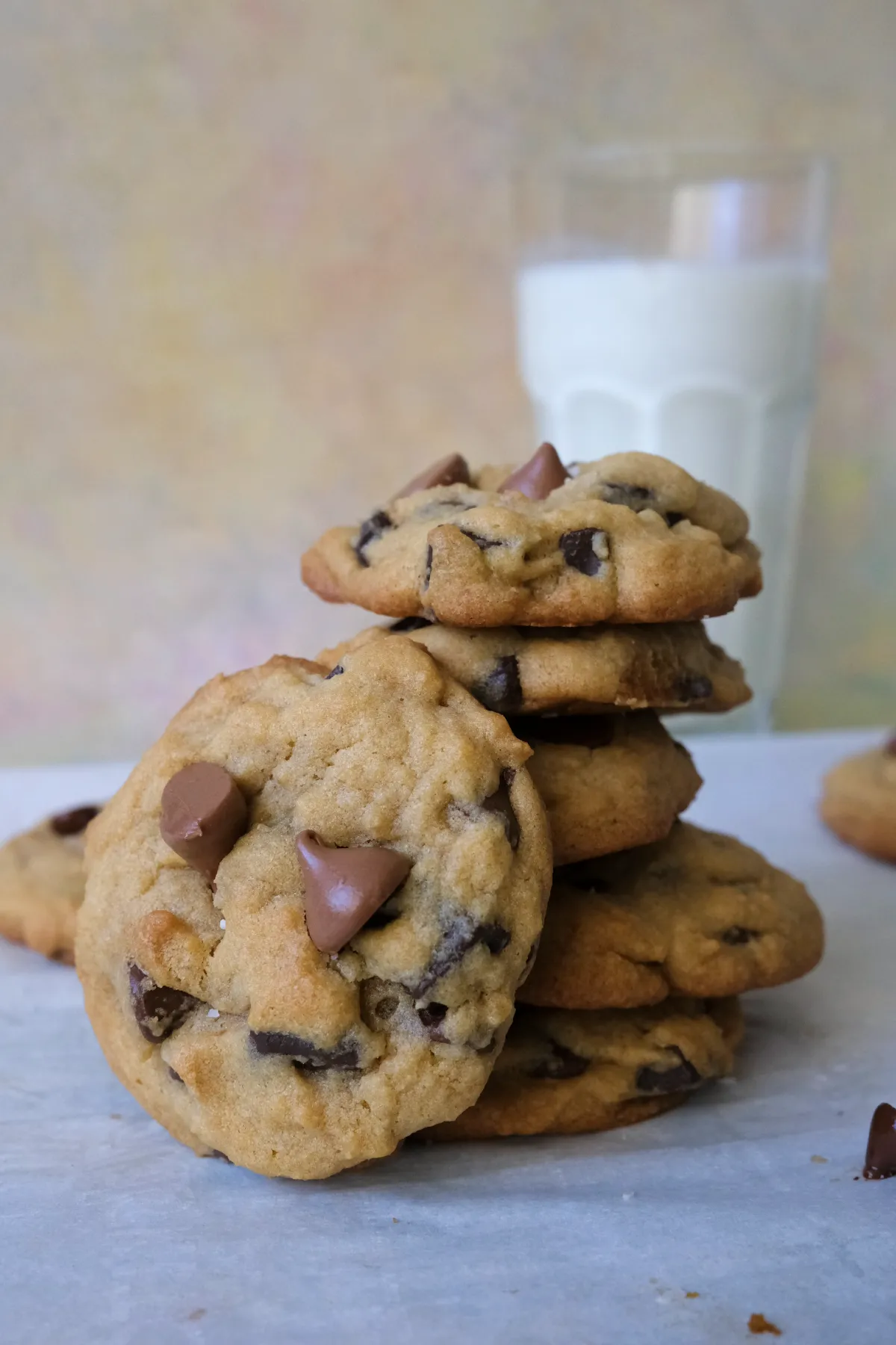Brown sugar chocolate chip cookies stacked on parchment paper with a glass of milk in the background.
