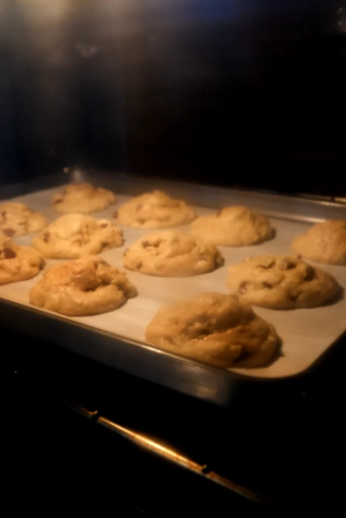 Chocolate chip cookies baking in the oven on a parchment-lined metal baking sheet.