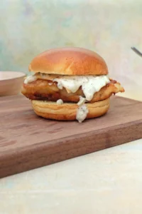 Crispy cod fish sandwich with tartar sauce and cheese on a toasted brioche bun.