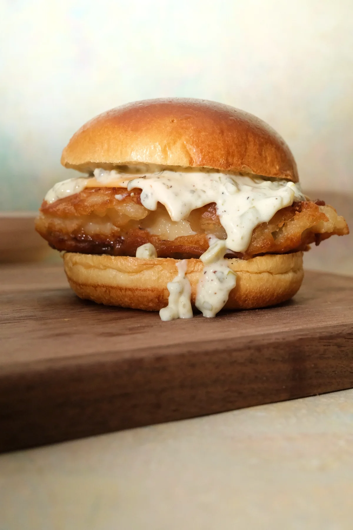 Crispy cod fish sandwich with tartar sauce and cheese on a toasted brioche bun.