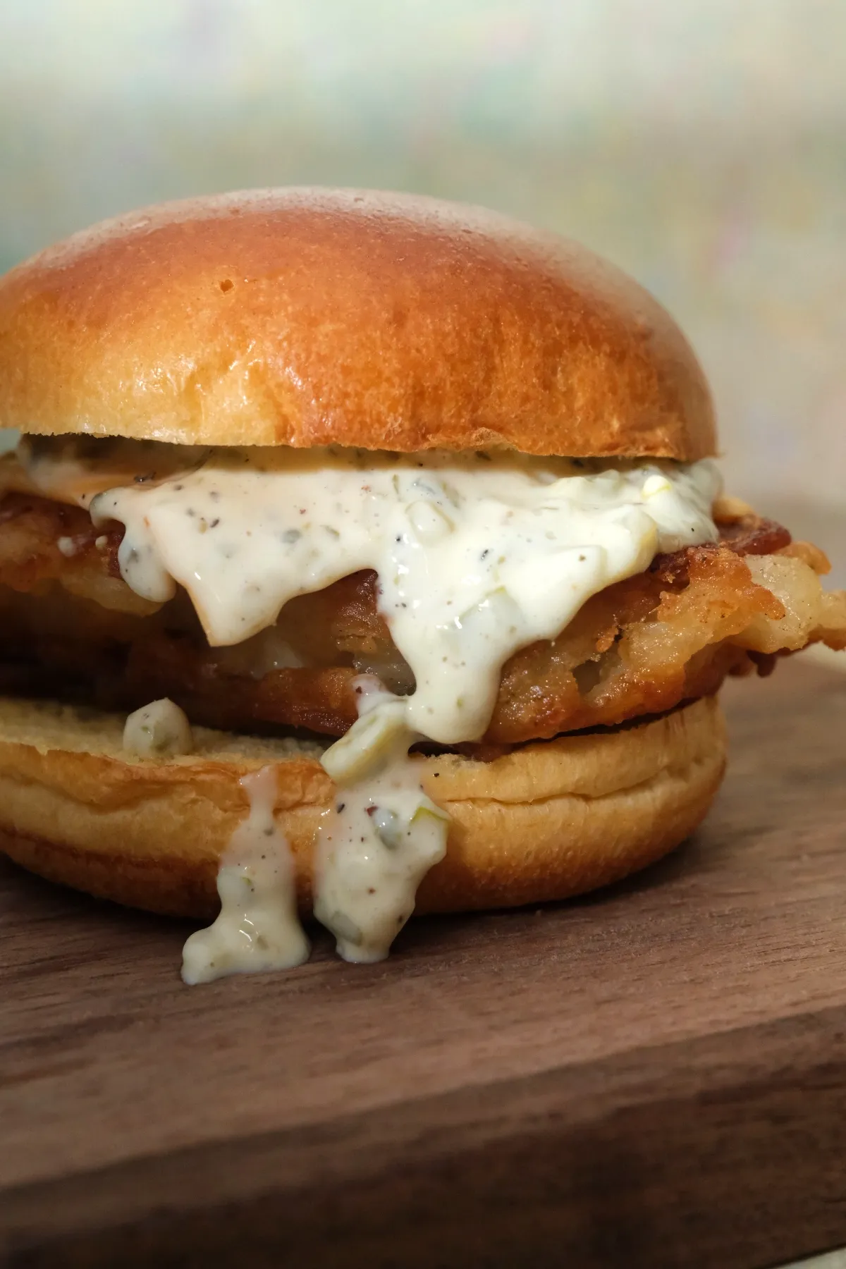 Close-up of a crispy battered cod fish sandwich with homemade tartar sauce on a toasted brioche bun.