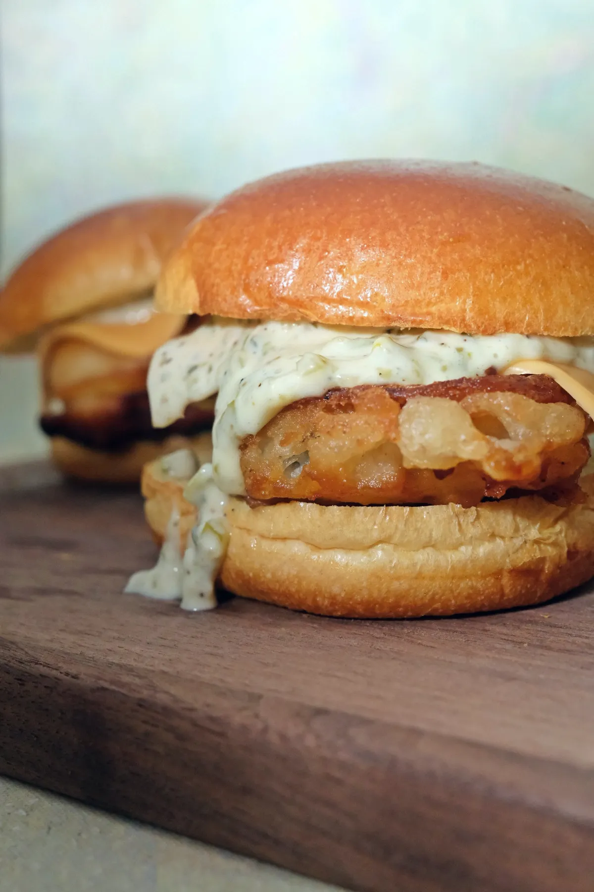 Two crispy cod fish sandwiches on brioche buns with tartar sauce on a wooden board.