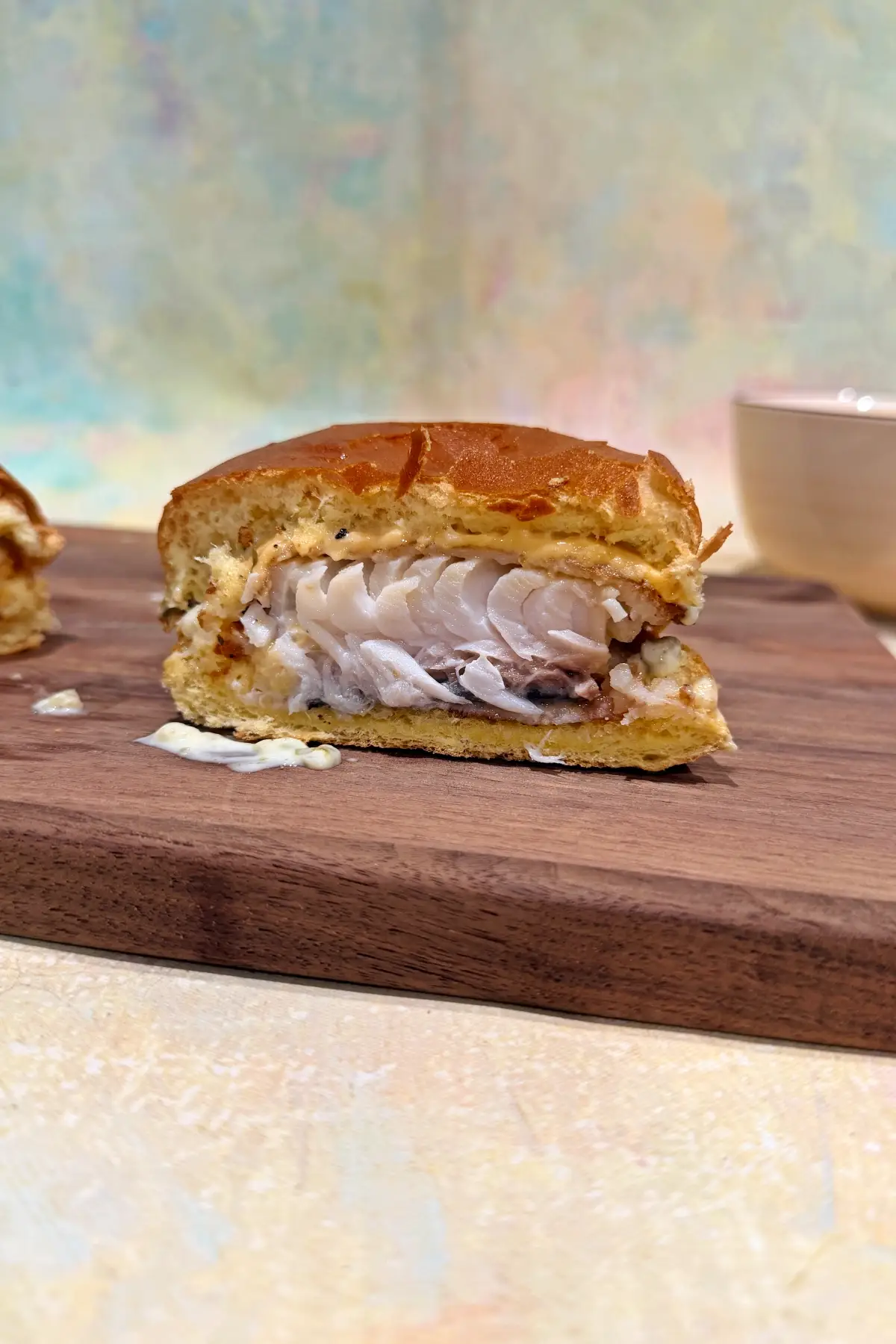 Half of a cod fish sandwich showing flaky white fish inside crispy batter on a brioche bun.