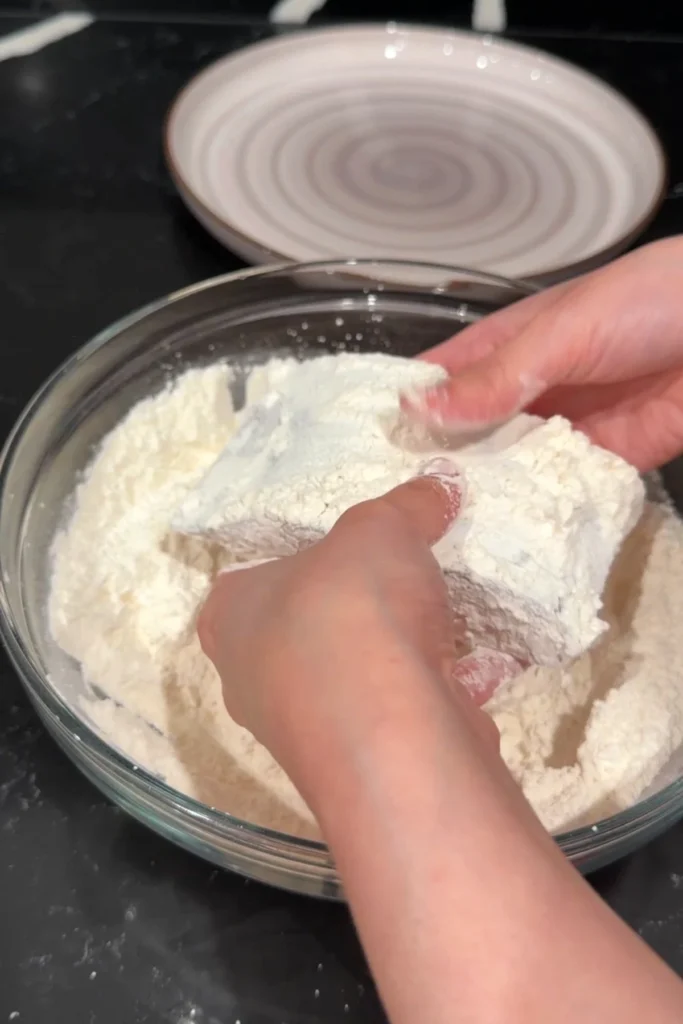 Dredging cod fillet in seasoned flour mixture before making the batter.