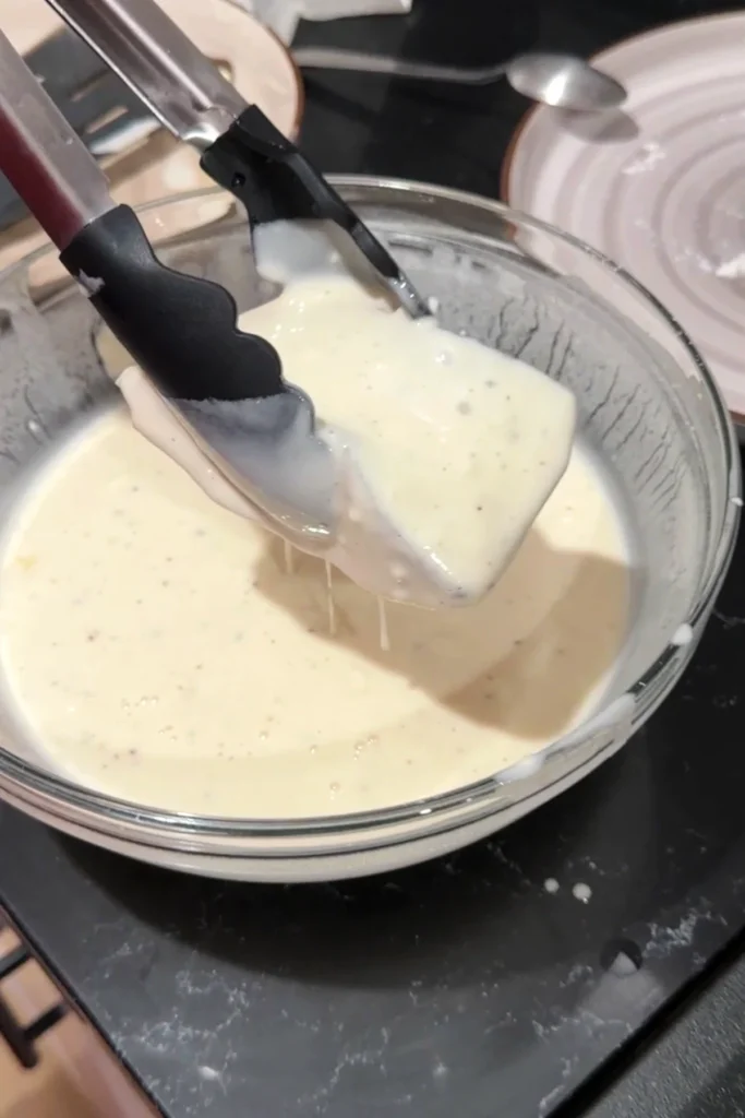 Cod fillet coated in smooth batter before frying.