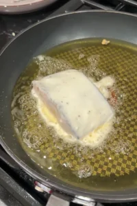 Battered cod fillet frying in hot oil in a skillet.