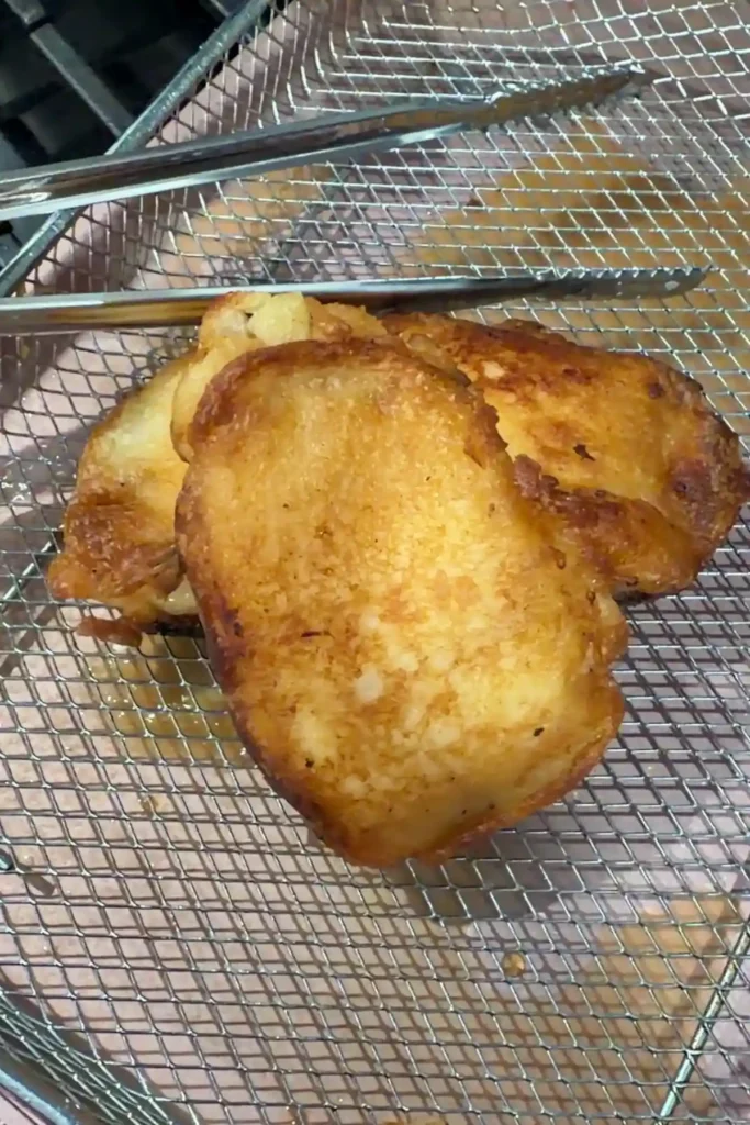 Golden fried cod fillets resting on a wire rack after frying.
