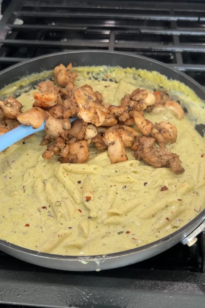 Cooked chicken being added back into creamy pesto pasta