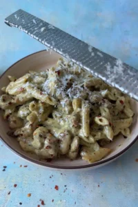 Fresh parmesan cheese being grated over creamy pesto chicken pasta