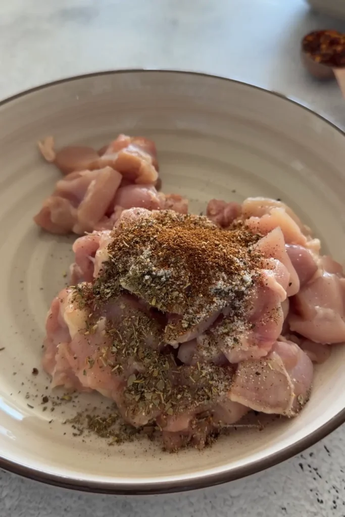 Raw chicken pieces in a bowl seasoned with salt, pepper, paprika, and dried herbs