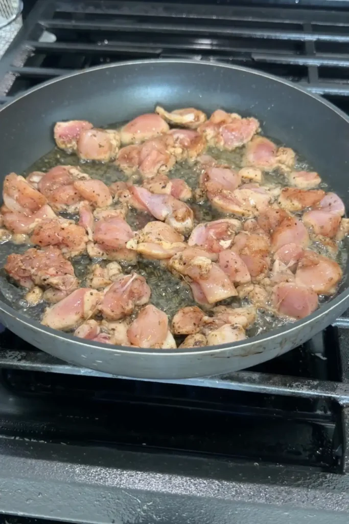 Chicken pieces cooking in a skillet with oil, starting to turn opaque