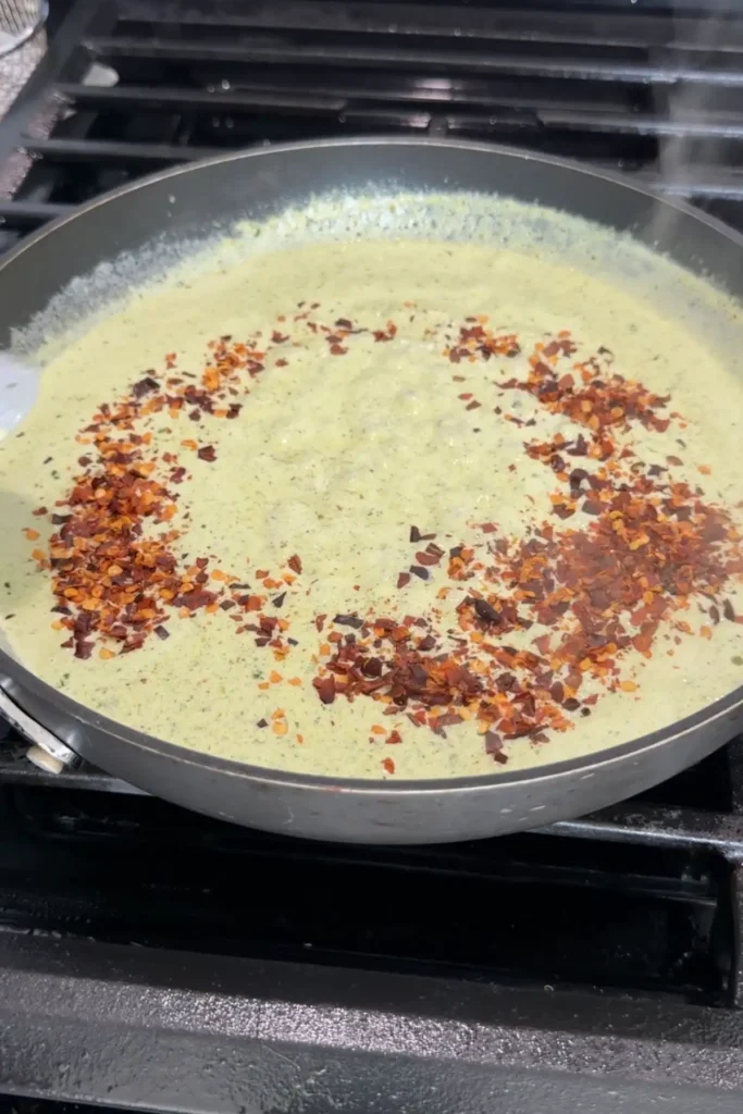 Creamy pesto sauce with red pepper flakes sprinkled on top for heat