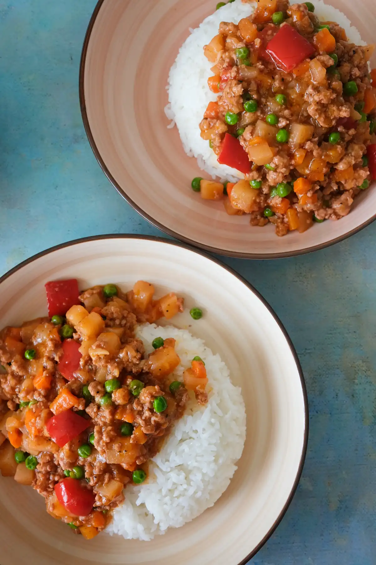 Two plates of Filipino pork picadillo served over white rice on a blue background.