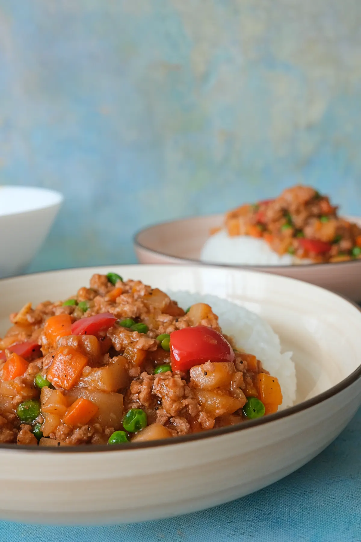 Bowl of Filipino pork picadillo with potatoes, carrots, peas, and bell peppers in savory sauce.