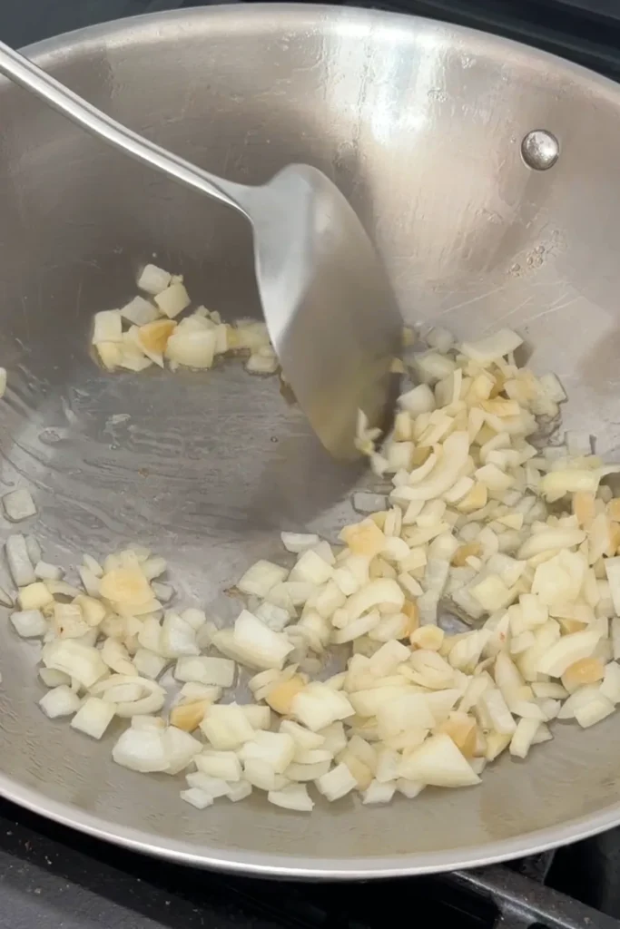 Diced onions and garlic sautéing in oil in a large pan.