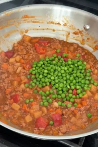 Green peas added to Filipino pork picadillo in skillet.