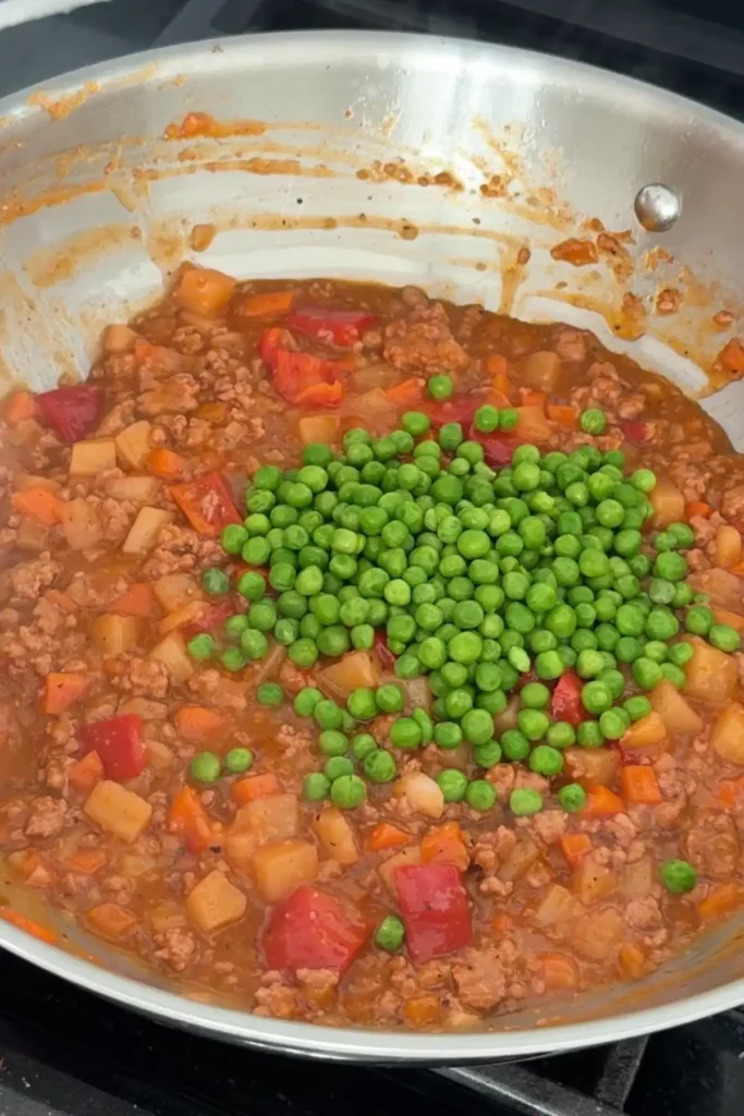 Green peas added to Filipino pork picadillo in skillet.